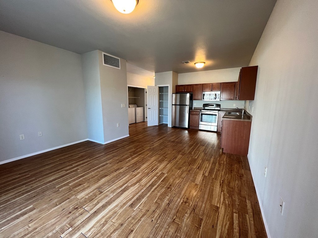 an empty living room with wood flooring and a kitchen